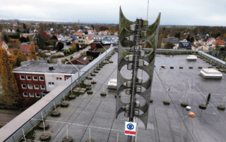 Große, moderne Sirenenanlage auf dem flachen Dach der Kreisverwaltung in Brake Die Sirene besteht aus mehreren übereinander angeordneten Lautsprechern. Das Dach ist weitläufig und mit technischen Aufbauten und Geländern versehen.