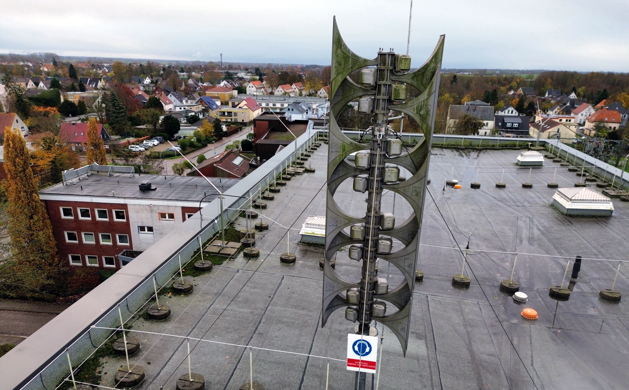 Große, moderne Sirenenanlage auf dem flachen Dach der Kreisverwaltung in Brake Die Sirene besteht aus mehreren übereinander angeordneten Lautsprechern. Das Dach ist weitläufig und mit technischen Aufbauten und Geländern versehen.