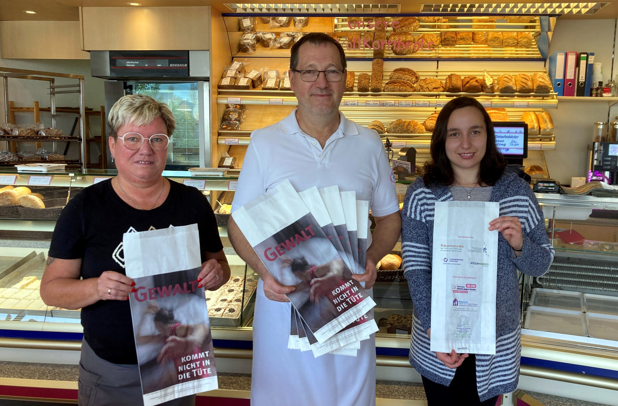 Klaus Wieting und zwei seiner Beschäftigten stehen in einer Bäckerei und präsentieren die Aktionsbrötchentüten.