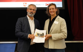 Timo Quander übergibt Larissa Jaegerdas Ladeinfrastrukturkonzept.