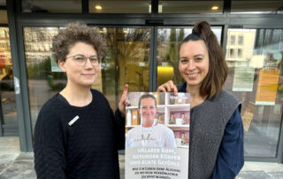 Anne Humboldt und Maren Ozanna stehen vor dem Kreishaus in Brake und präsentieren das Plakat zur Veranstaltung