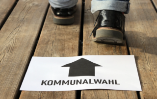 Holzboden mit weissem Blatt auf dem ein schwarzer Richtungspfeil und das Wort Kommunalwahl liegt