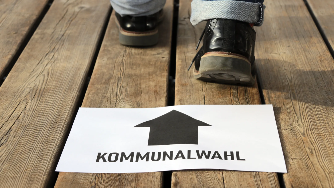 Holzboden mit weissem Blatt auf dem ein schwarzer Richtungspfeil und das Wort Kommunalwahl liegt